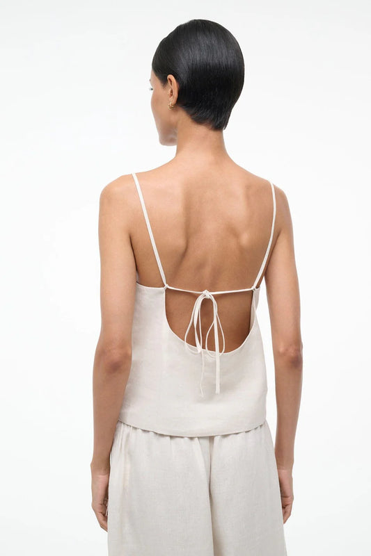 Woman wearing a white sleeveless top with thin straps and open back on a white background