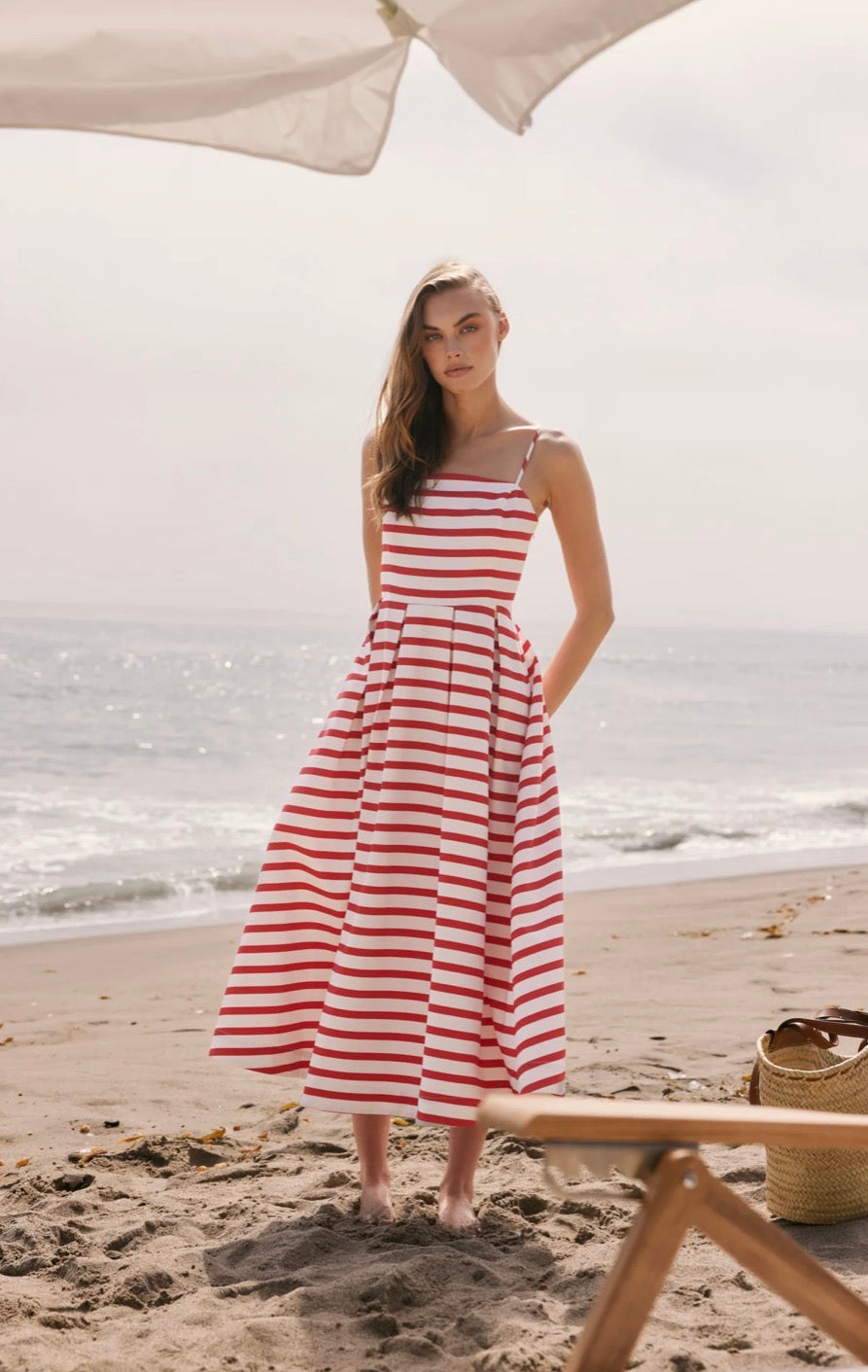 Woman in a red and white striped dress standing on a beach with ocean in the background