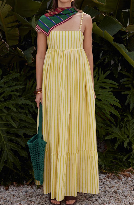 Woman in a yellow dress holding a green bag against a leafy background