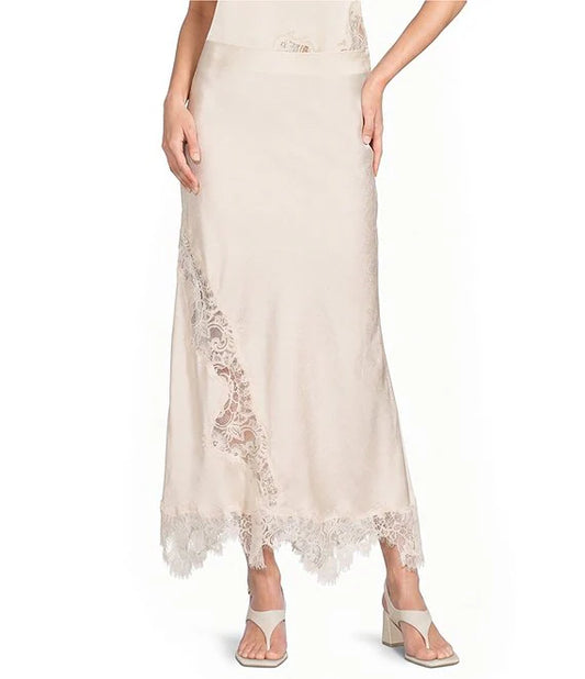 A model wearing a light beige maxi skirt with delicate lace trim along the side and hem, paired with beige heeled sandals against a plain white background.