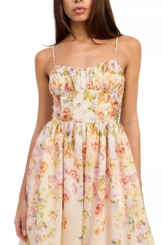 A woman wearing a sleeveless floral midi dress with thin spaghetti straps, a gathered sweetheart bodice, and a flared skirt. The dress features a soft cream base with a multicolor floral pattern in pink, yellow, and green, set against a plain white background.