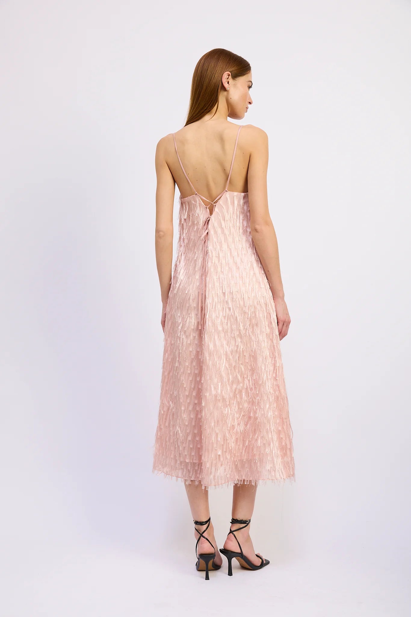 Woman wearing a pink lace dress with thin straps on a white background