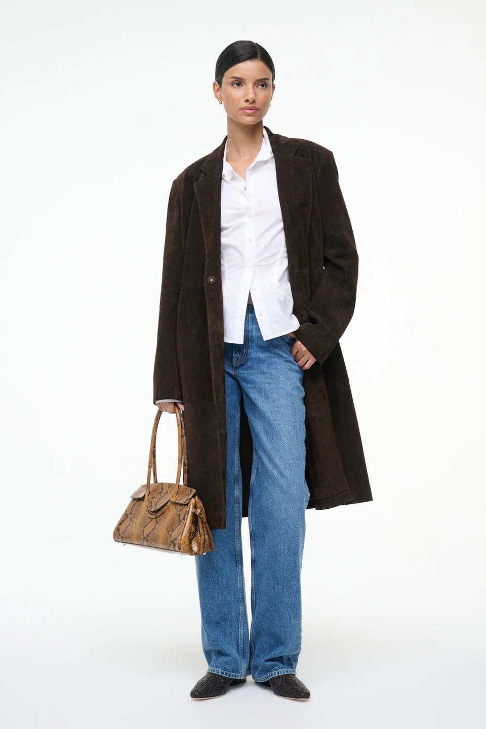 Woman wearing a brown coat, white shirt, blue jeans, and holding a brown handbag on a white background