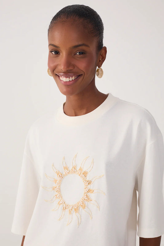 Woman wearing a white sweater with a sun design on a plain background