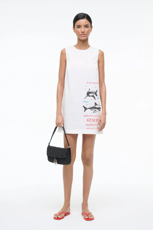 Woman wearing a white sleeveless dress with two shark swim graphic and holding a black handbag on a white background