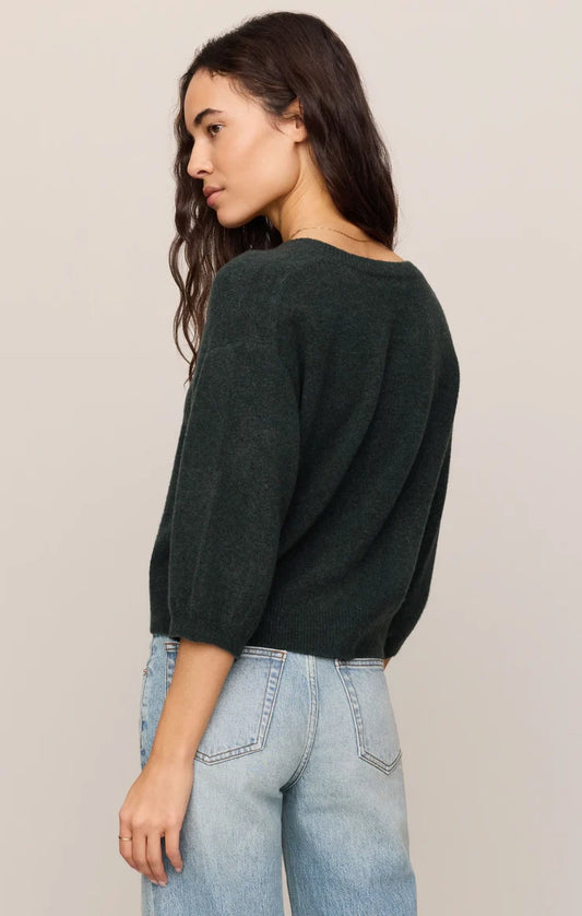 Woman wearing a dark green sweater and light blue jeans against a plain background