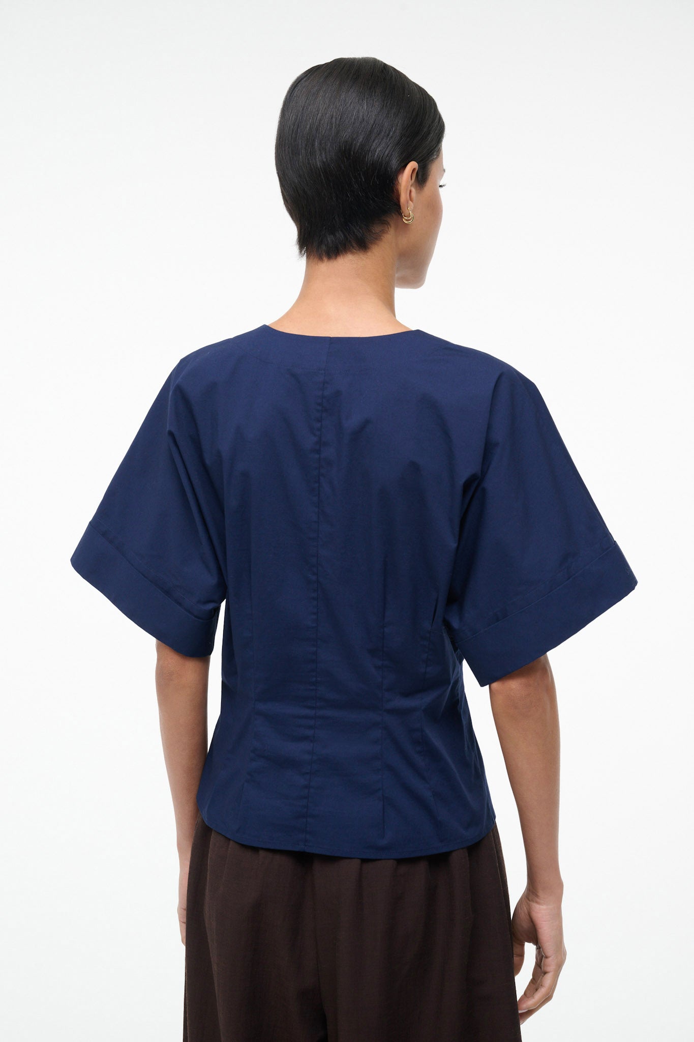 Person wearing a navy blue top and brown pants on a white background