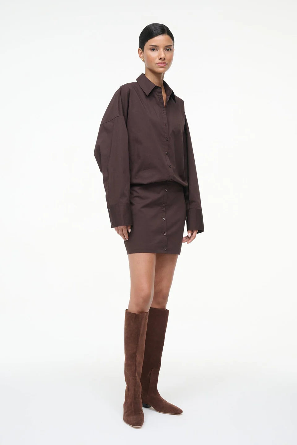 Woman wearing a brown oversized shirt and skirt with knee-high brown boots on a white background