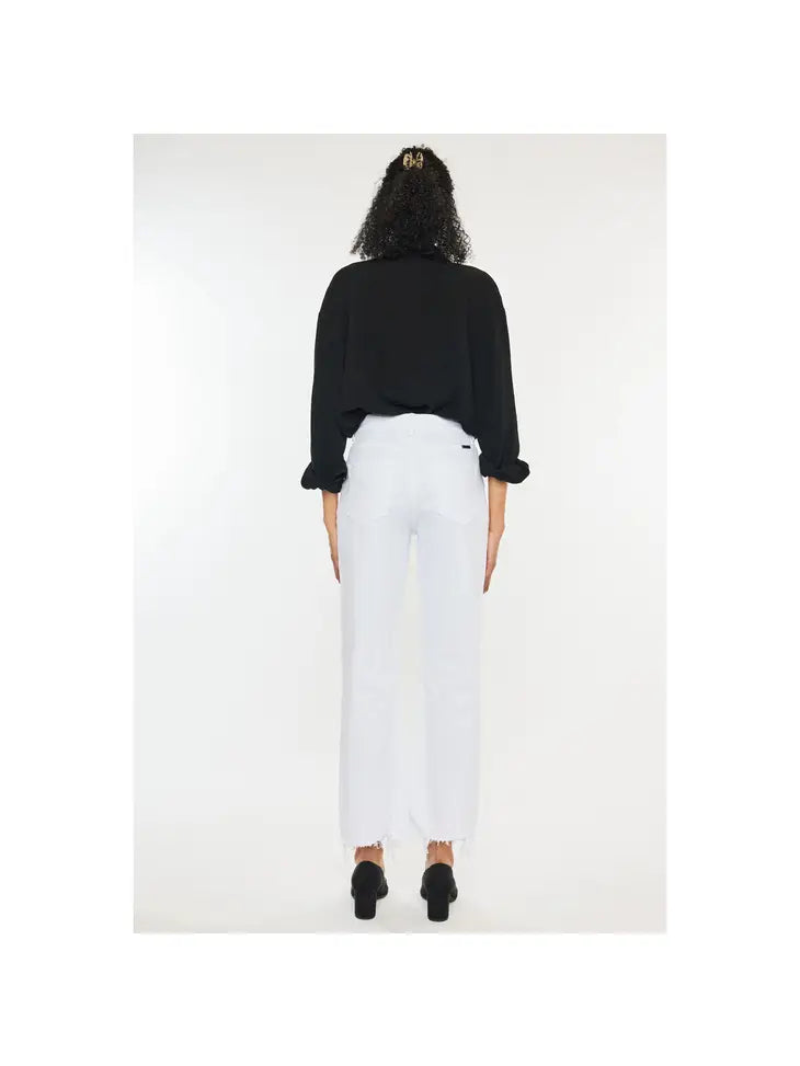 Woman wearing white high rise denim jeans with a frayed bottom hem wearing a black polo and high heels.