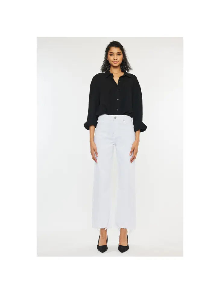 Woman wearing white high rise denim jeans with a frayed bottom hem wearing a black polo and high heels.
