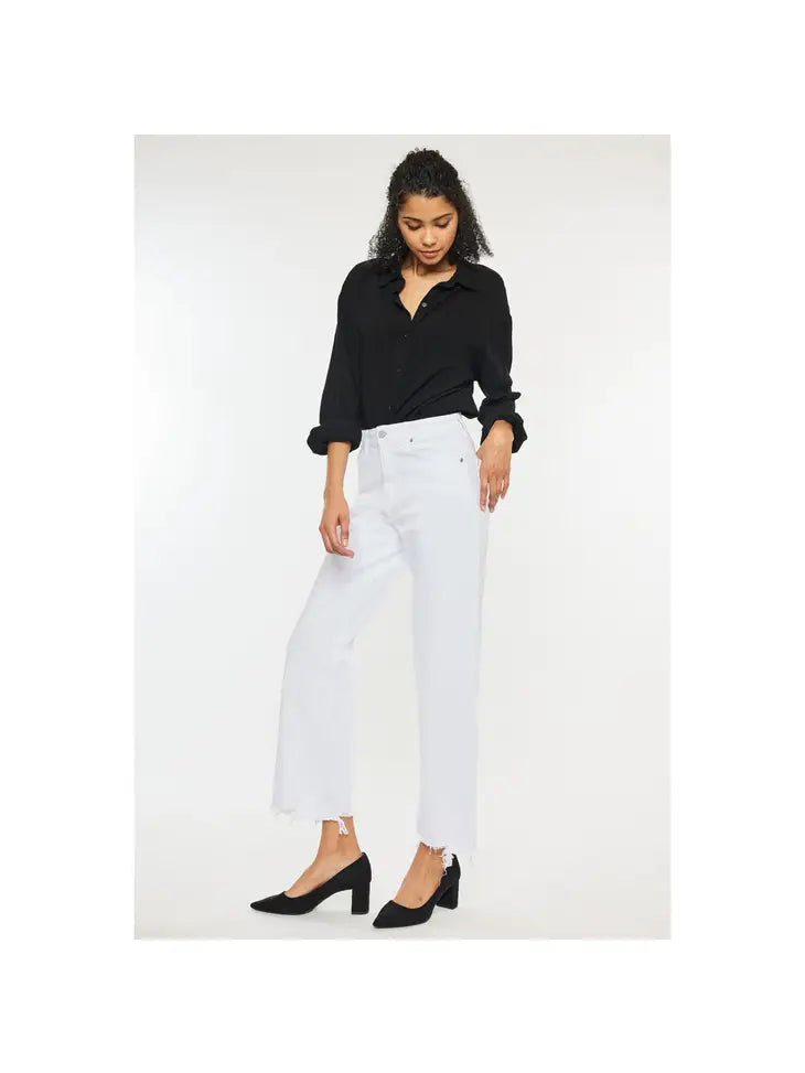 Woman wearing white high rise denim jeans with a frayed bottom hem wearing a black polo and high heels.