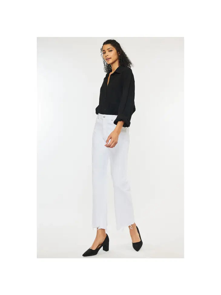 Woman wearing white high rise denim jeans with a frayed bottom hem wearing a black polo and high heels.