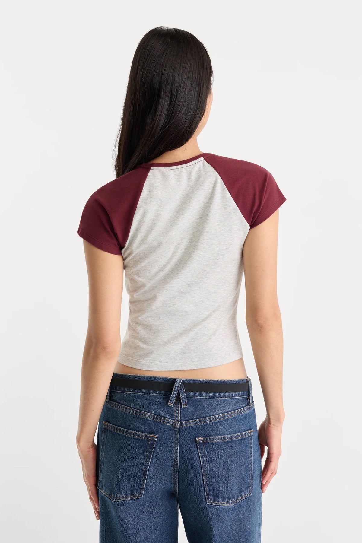 Person wearing a two-tone shirt with maroon sleeves and gray torso, paired with blue jeans on a white background.
