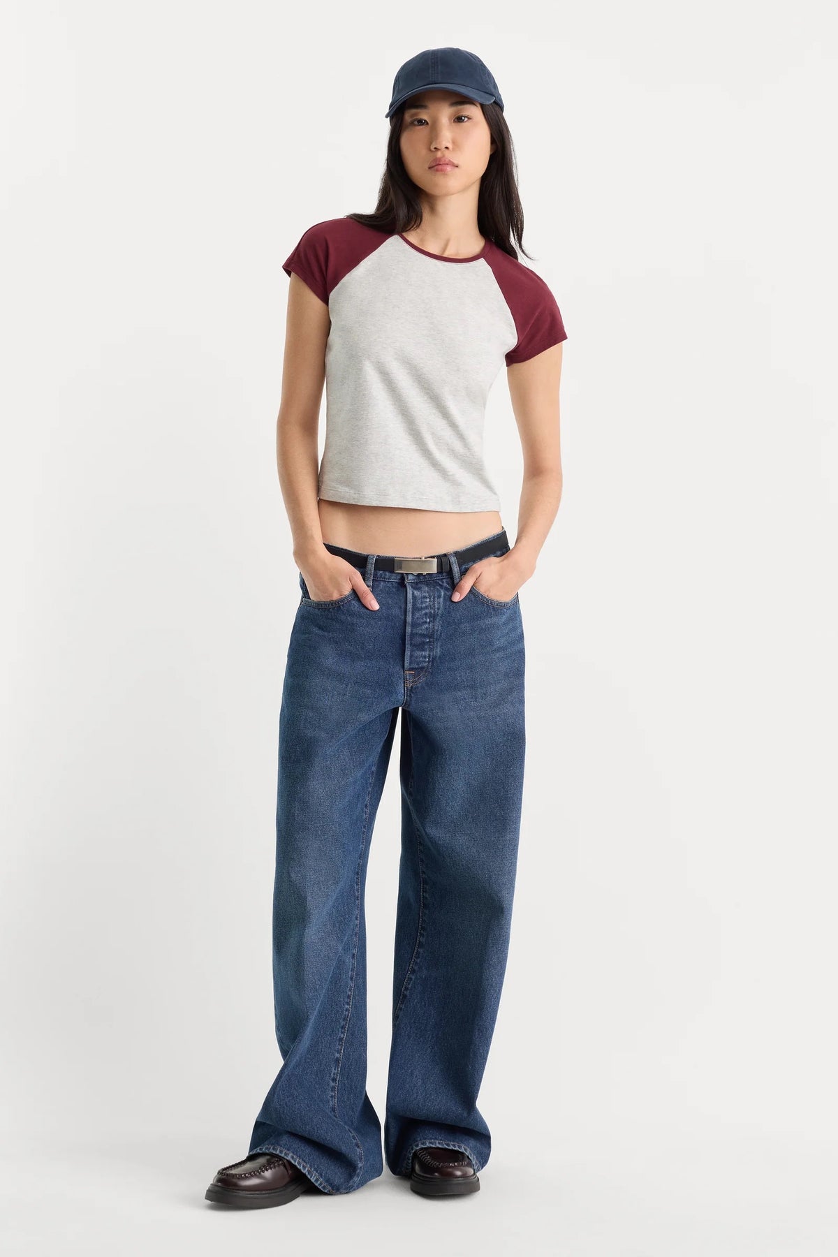 Person wearing a white and red baseball shirt with blue jeans on a white background