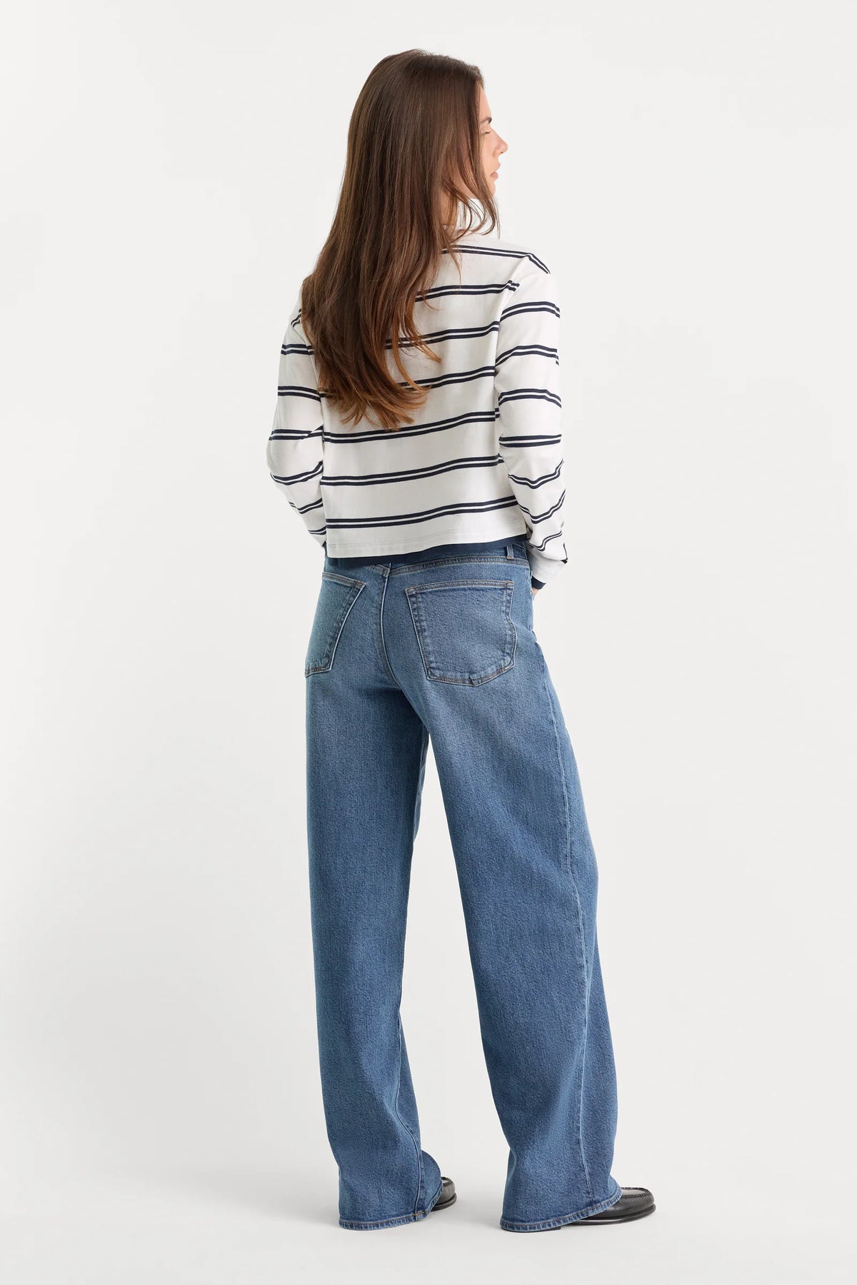 Person wearing a striped shirt and blue jeans on a white background