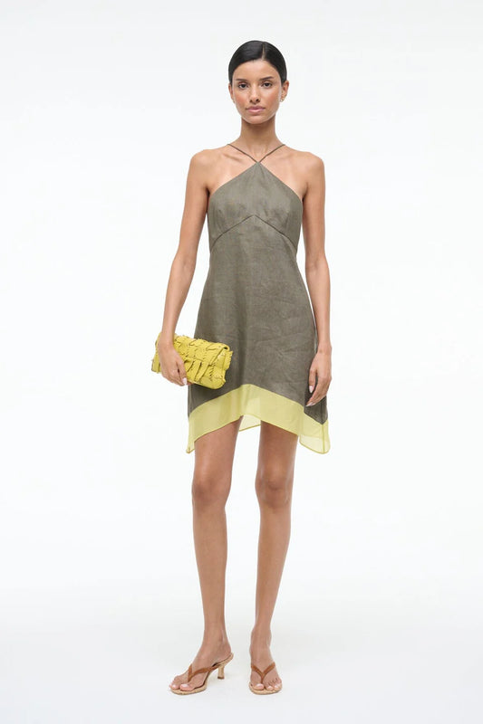 Woman wearing a green and yellow dress with a yellow clutch on a white background