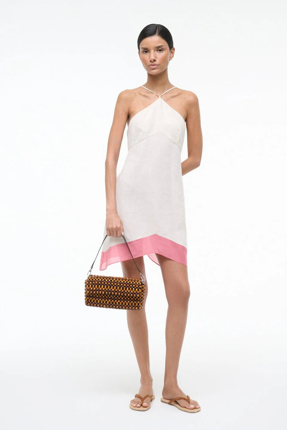 Woman wearing a white dress with a pink hem holding a woven handbag on a white background
