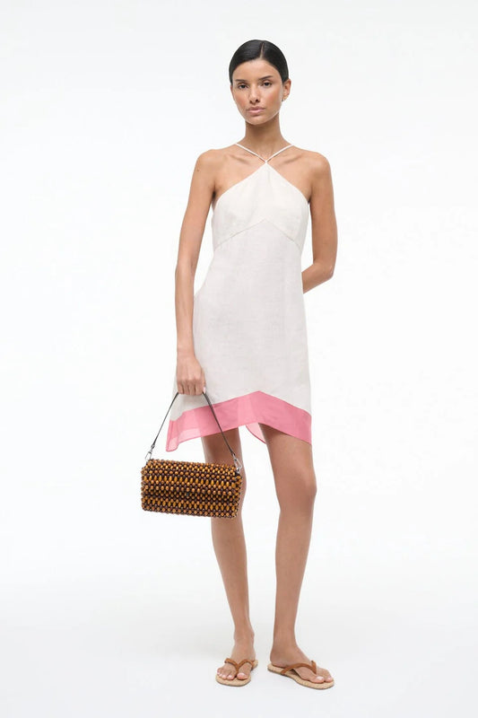 Woman wearing a white dress with a pink hem holding a woven handbag on a white background