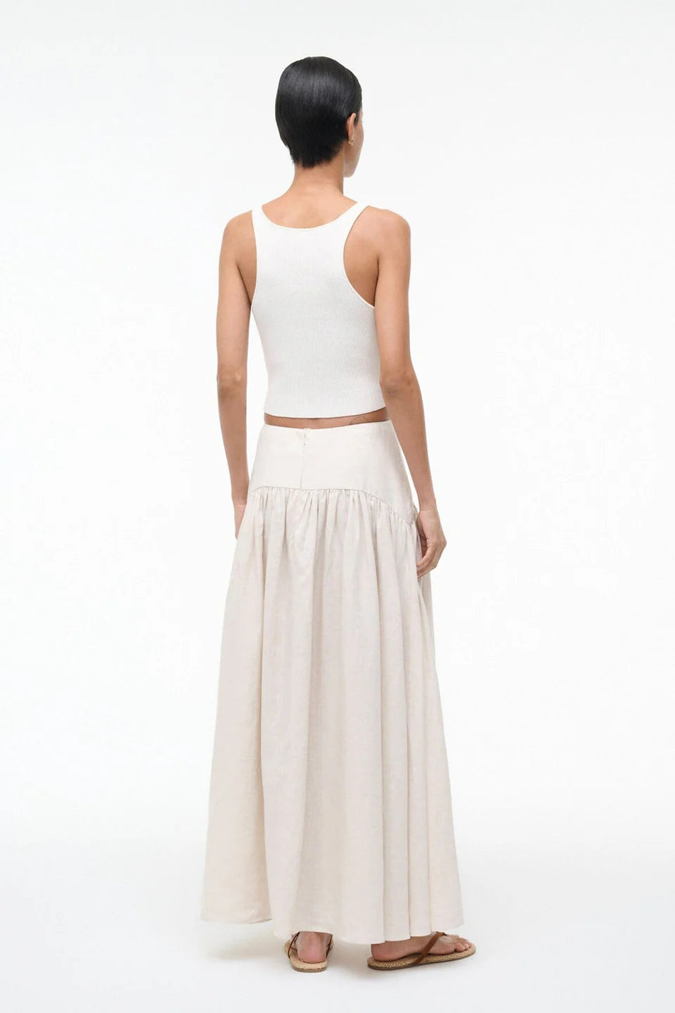 Woman wearing a white sleeveless top and beige skirt on a white background