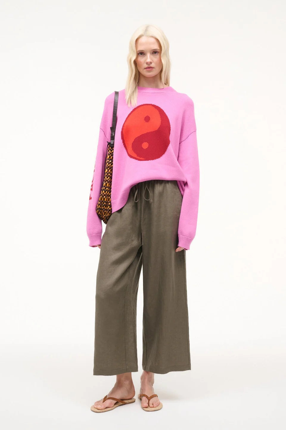 Person wearing a pink sweater with a red circle design, standing against a white background