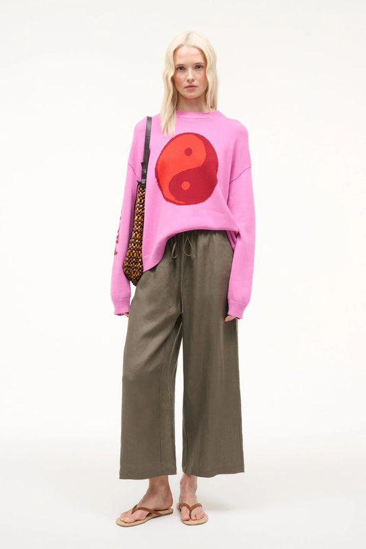 Person wearing a pink sweater with a red circle design, standing against a white background