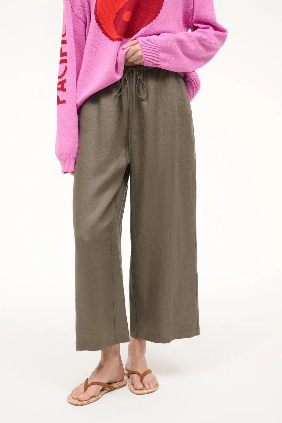 Person wearing a pink sweater and brown pants on a white background