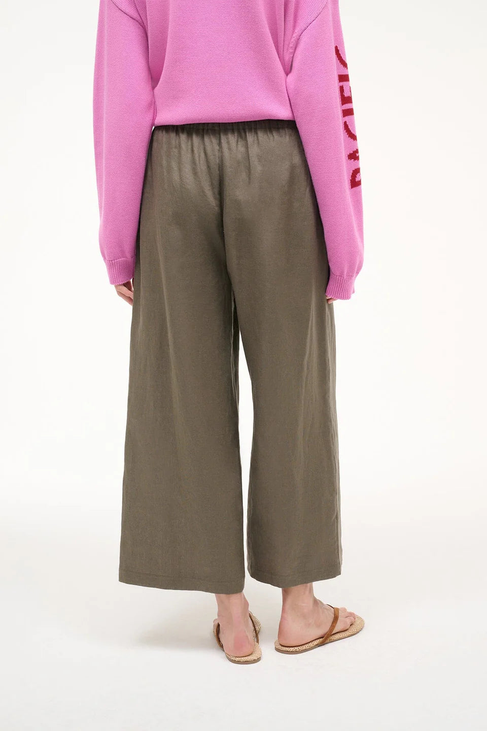 Person wearing a pink sweatshirt and olive green pants on a white background