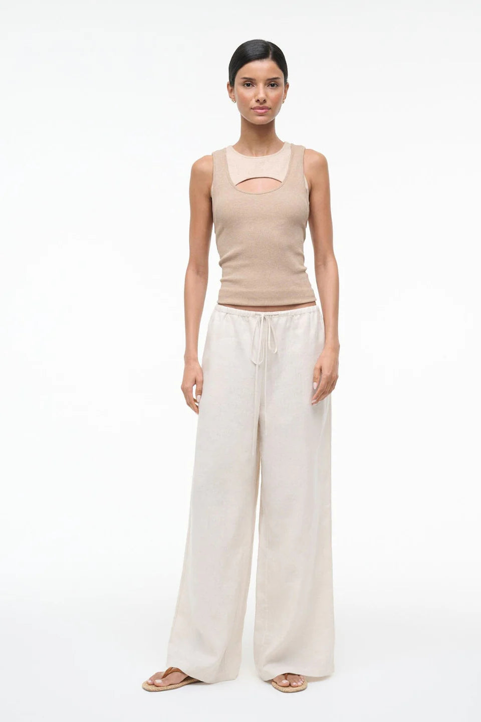 Woman wearing a beige sleeveless top and white wide-leg pants on a white background