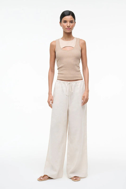 Woman wearing a beige sleeveless top and white wide-leg pants on a white background