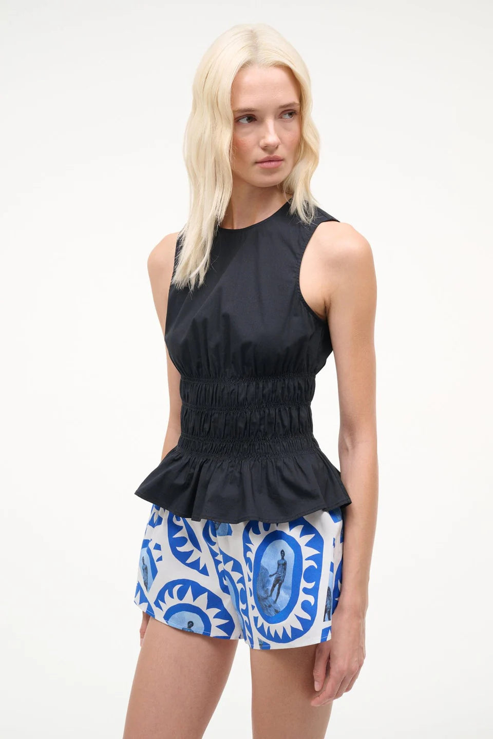 Woman wearing a black sleeveless top and patterned shorts on a white background