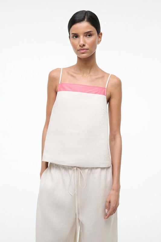 Woman wearing a white top with pink straps and beige pants on a white background