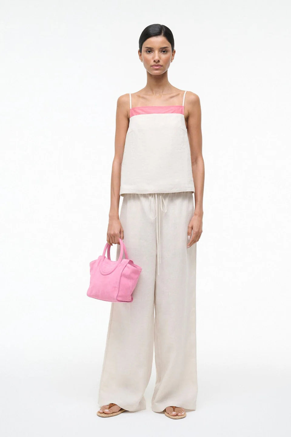 Woman holding a pink handbag wearing a white outfit with a pink top on a white background