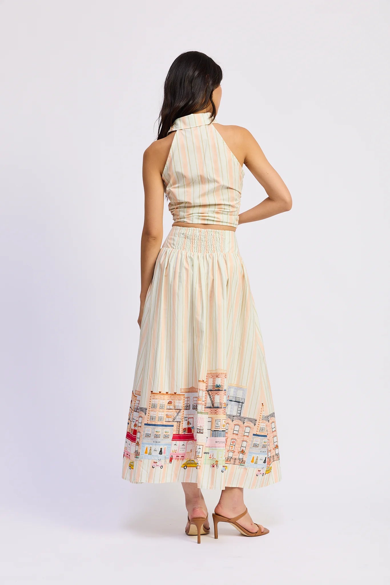 Woman wearing a cream-colored dress with a cityscape design on a white background