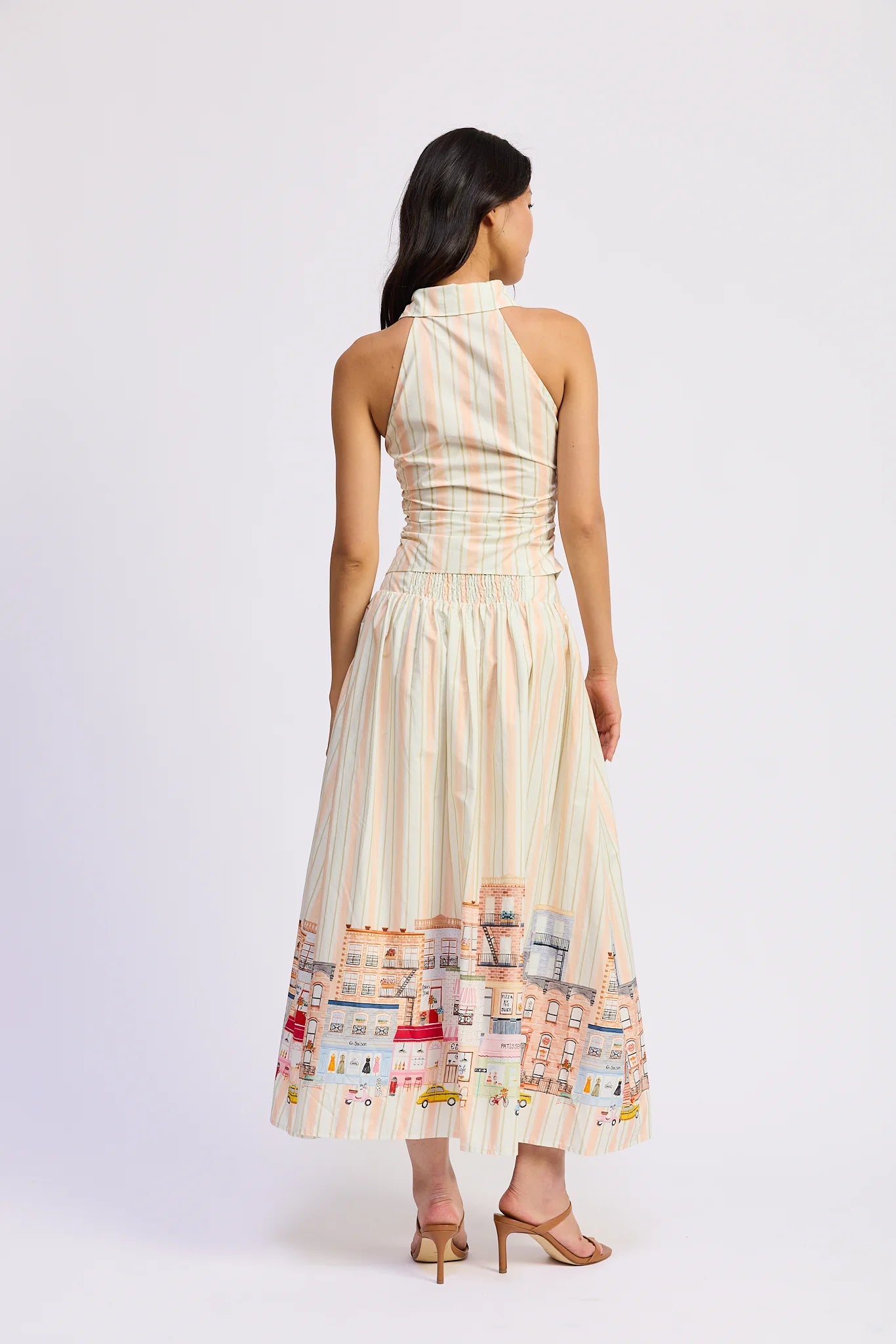 Woman wearing a long, light-colored dress with a patterned hem on a white background
