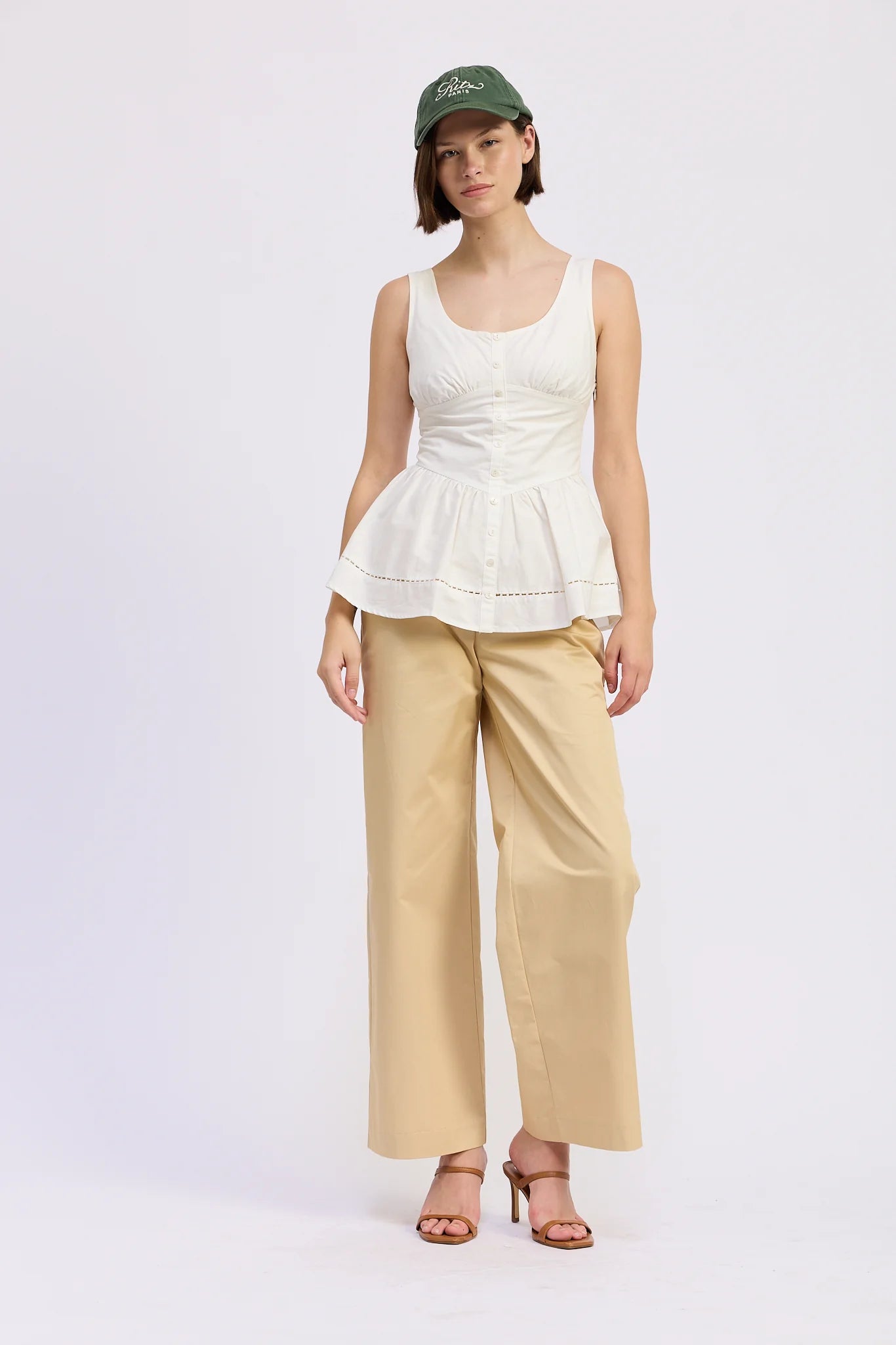 Woman wearing a white peplum top and beige pants on a white background