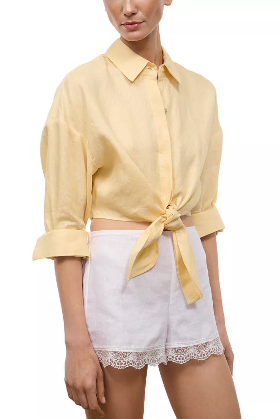 Woman wearing yellow button down top with tie front and white shorts.