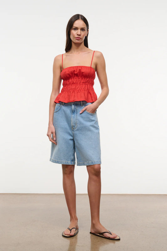 Woman wearing a red top and blue shorts on a plain background