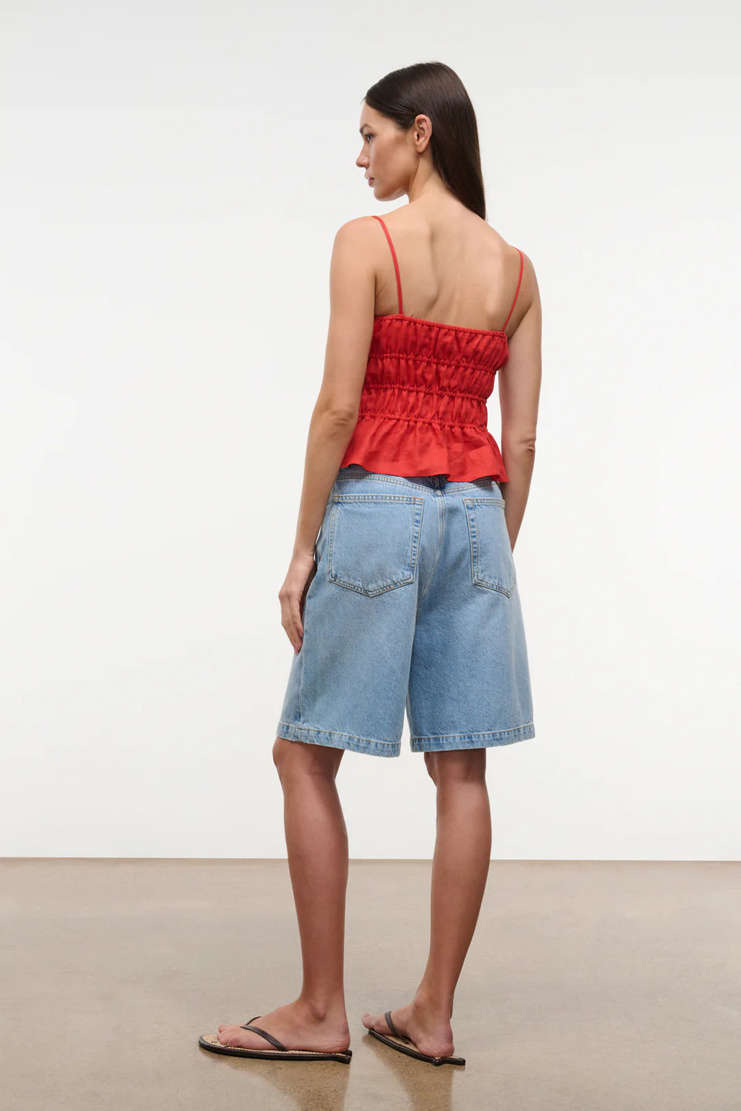 Woman wearing a red top and light blue denim shorts against a white background