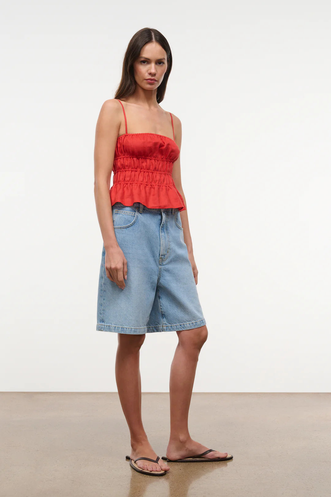 Woman wearing a red top and denim shorts on a plain background