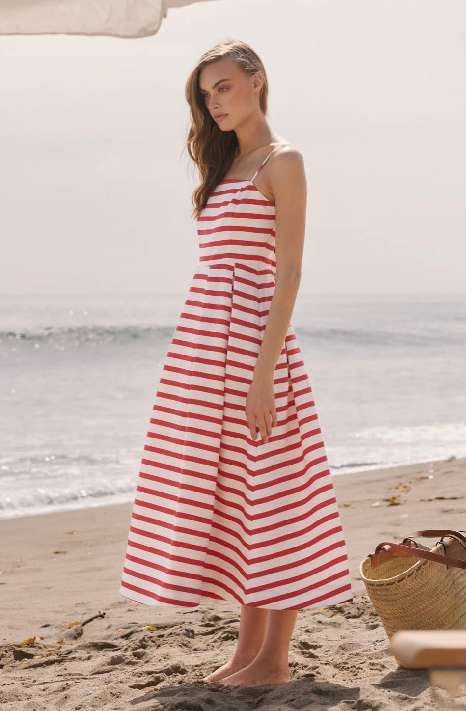 Woman in a red and white striped dress standing on a beach.