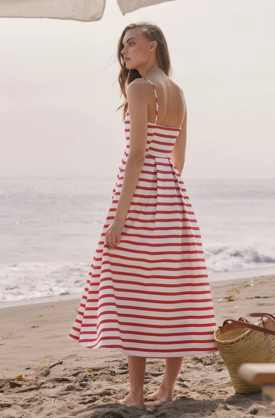 Woman in a red and white striped dress standing on a beach.