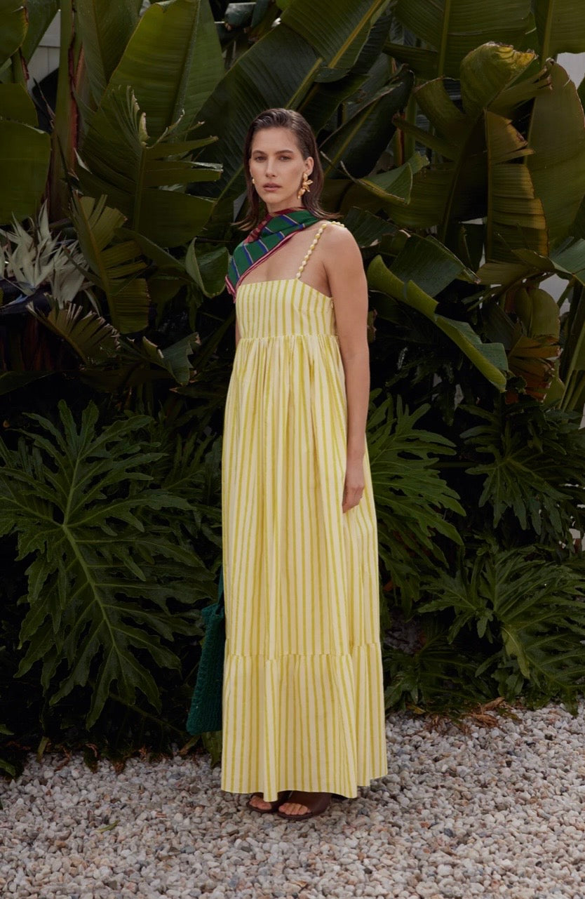 Woman in a yellow dress standing in front of green foliage