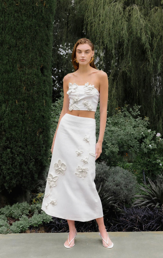 Woman wearing a white floral top and skirt set standing in a garden.