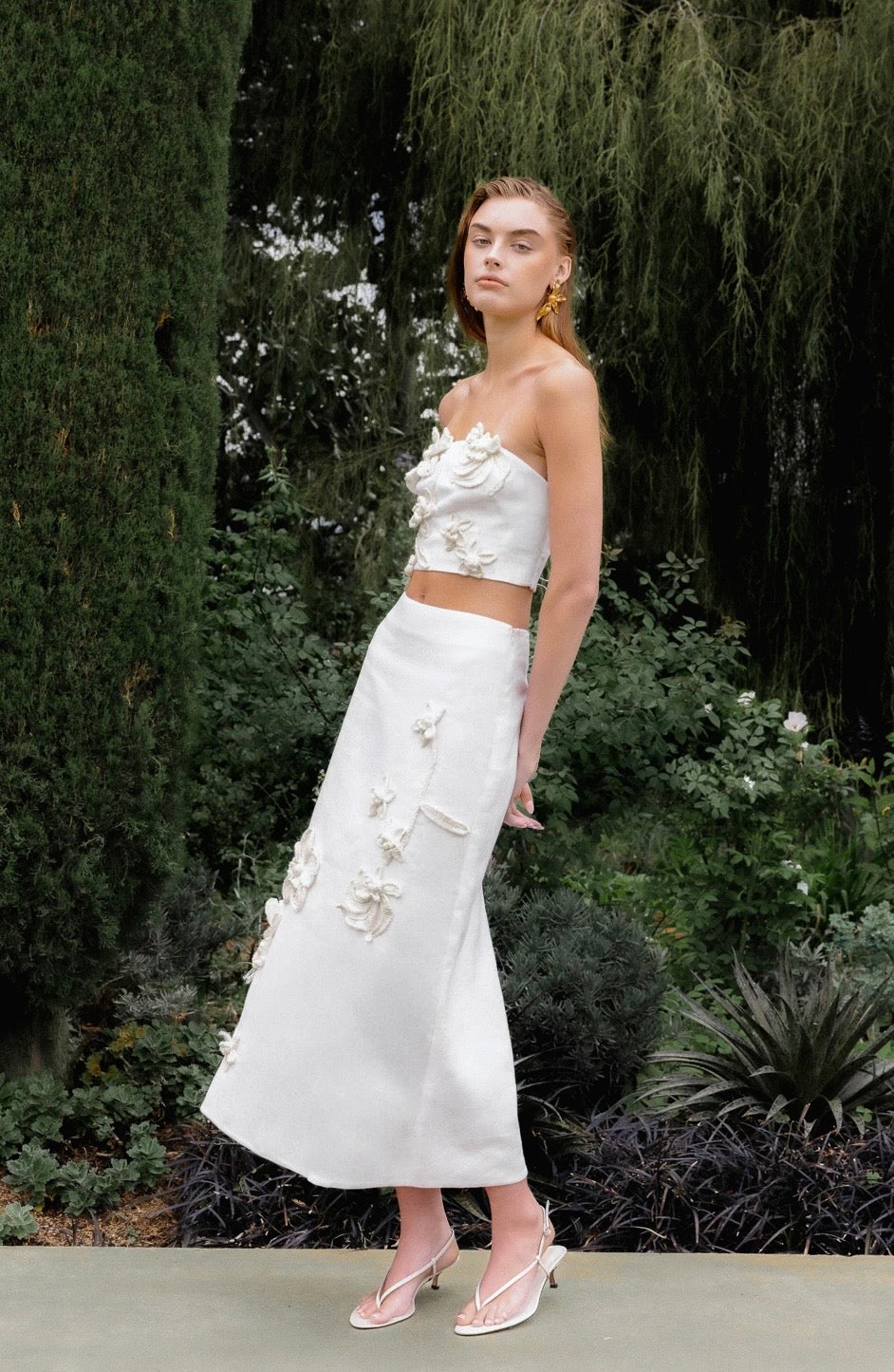 Woman in a white floral dress standing in a garden setting