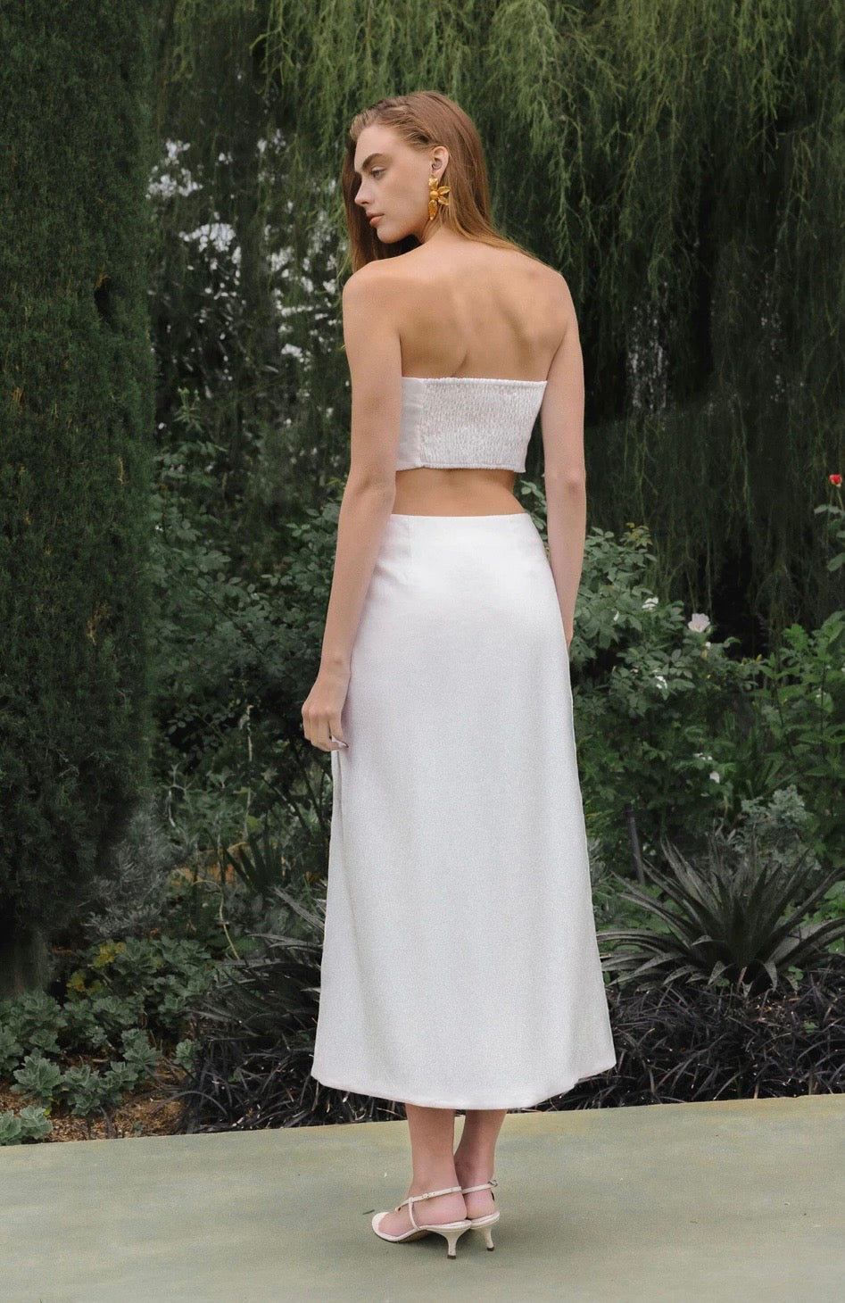 Woman wearing a strapless top and white skirt with a blurred natural background