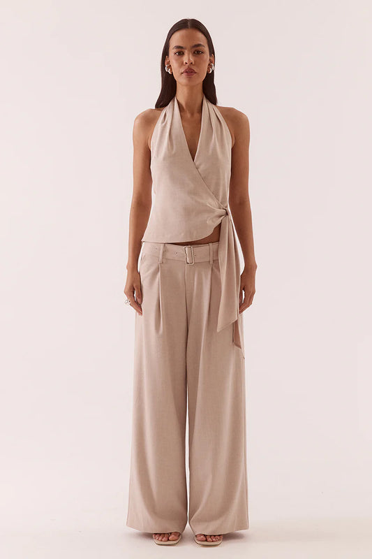 Woman wearing a beige halter top and wide-leg pants on a white background