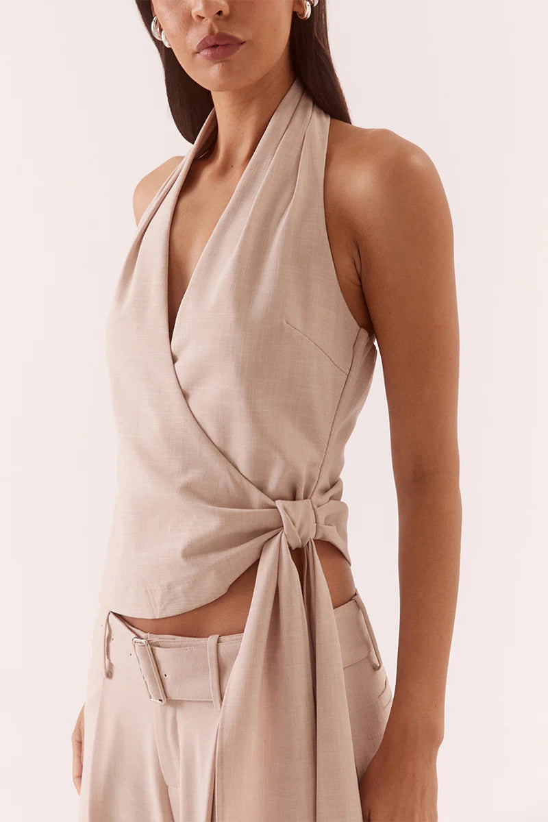 Woman wearing a beige halter top with a knot detail on a light pink background