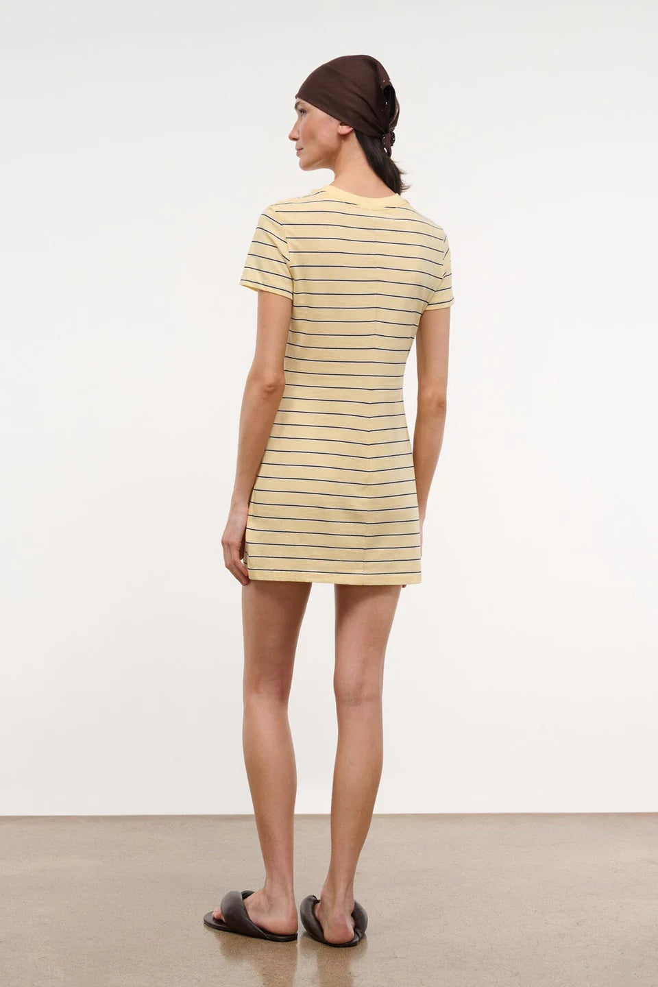 Woman wearing a yellow striped dress and brown headscarf on a white background