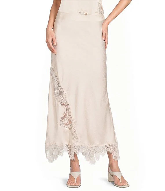 A model wearing a light beige maxi skirt with delicate lace trim along the side and hem, paired with beige heeled sandals against a plain white background.