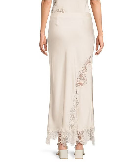 A woman modeling a floor-length cream satin skirt with delicate lace trim along the side and hem, shown against a plain white background.